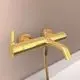 Wandmontierte Badarmatur in Brushed Gold mit einem Wasserhahn und einem Brauseschlauch, hergestellt von Ideal Standard.